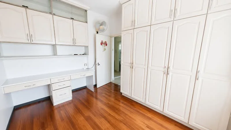 Room features: light wood flooring, built-in wardrobe with white doors, white cabinetry with glass panels, desk with drawers, wall-mounted fan, neutral wall color, doorway leading to another room; style: modern.