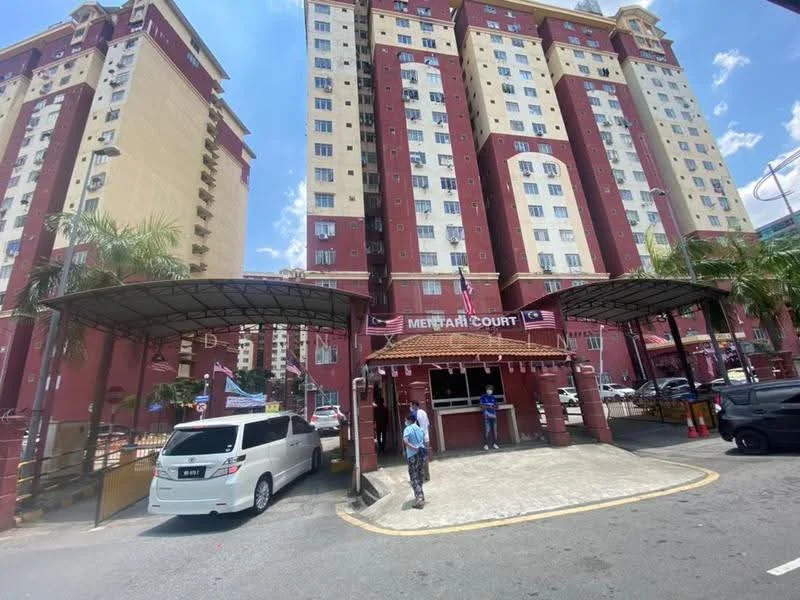 Exterior type: low-rise apartment block; features: red and cream painted facade, covered car porch, main entrance with signage, surrounded by palm trees, multiple storeys visible, parking area, security guard station, open-air parking, urban context with nearby buildings; style: modern.