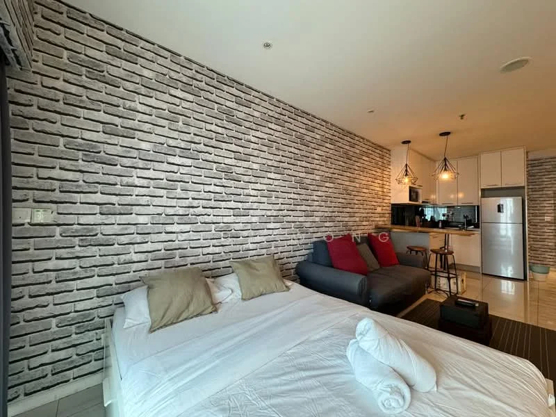 Room features: grey exposed brick accent wall, white painted walls, white bedding with pillows, 2 beige decorative pillows, grey fabric sofa, red accent cushions on sofa, wooden coffee table, pendant lighting fixtures, kitchenette with black countertop, stainless-steel refrigerator, built-in microwave, kitchen cabinets, tile flooring; style: modern.