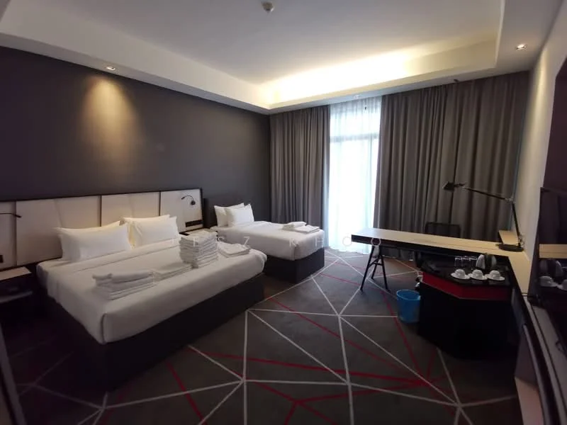 Bedroom features: two beds with white linens, upholstered headboard, grey accent wall, floor-to-ceiling windows with sheer curtains, desk with black chair, wall-mounted TV, carpet flooring with geometric pattern, table lamp, buckets for cleaning supplies, decorative items on desk; style: modern.