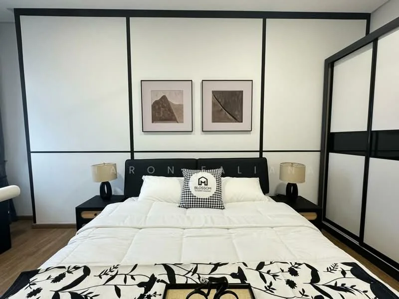 Bedroom features: king-size bed with white bedding, black and white decorative throw blanket, two bedside lamps with beige shades, framed artwork on walls, black accent wall with white panels, wooden flooring, built-in wardrobe with sliding doors, decorative pillows; style: modern.