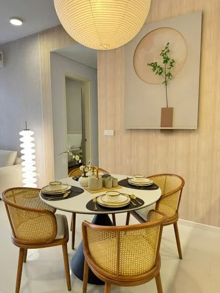Dining features: round dining table, white tabletop, black base, 4 rattan dining chairs, decorative vase with flowers, table setting with plates and cutlery, wall art with circular design, light wood accent wall, pendant light fixture, white ceramic vase; style: modern.