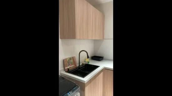 Kitchen features: single-bowl black sink, chrome pull-down faucet, white countertop, wood cabinetry with light finish, upper cabinets, lower cabinets, kitchen utensils on countertop, black dish rack; style: modern.