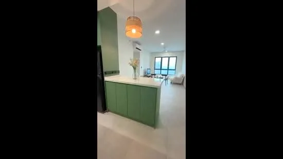 Kitchen features: green cabinetry, white countertop, pendant light, stainless-steel fridge, open layout to living area, tile flooring, wall-mounted split AC, decorative vase with flowers; style: modern; view: city. Living features: sofa, coffee table, floor-to-ceiling windows, natural light, light-colored walls; style: modern; view: city.