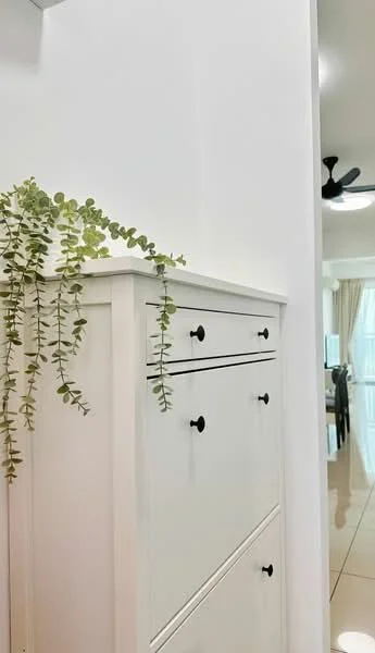Room features: white painted walls, light-colored cabinetry, black drawer handles, decorative plant, glossy tile flooring, ceiling fan, dining area visible in background, curtains in soft fabric; style: modern.