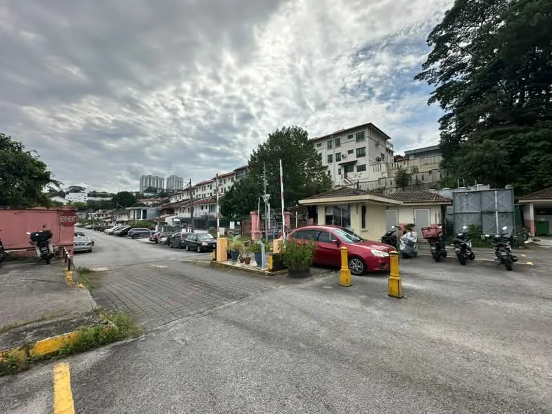 Exterior type: low-rise apartment block; features: multiple parking spaces, guard house at entrance, boom gate, surrounded by mature greenery, paved driveway, residential buildings in background, motorcycle parking, landscaped planters; style: modern.