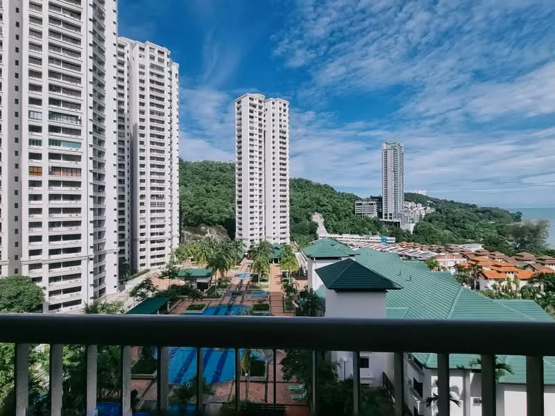 Exterior type: high-rise condominium; features: multiple high-rise buildings, green hillside in background, swimming pools visible, landscaped gardens, sea view, residential area with low-rise buildings, blue sky with scattered clouds; style: modern.