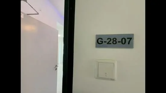Room features: white painted walls, grey door, numbered door sign, light switch.