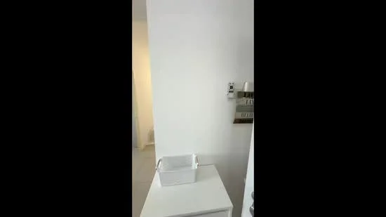 Room features: white painted walls, light-colored flooring, small white storage basket, wall-mounted storage rack, light switch, doorway leading to another room.
