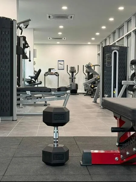 Room features: gym equipment, dumbbell, weight bench, treadmill, exercise bike, multi-gym machine, mirrored wall, recessed LED downlights, rubber flooring, air conditioning unit; style: modern.