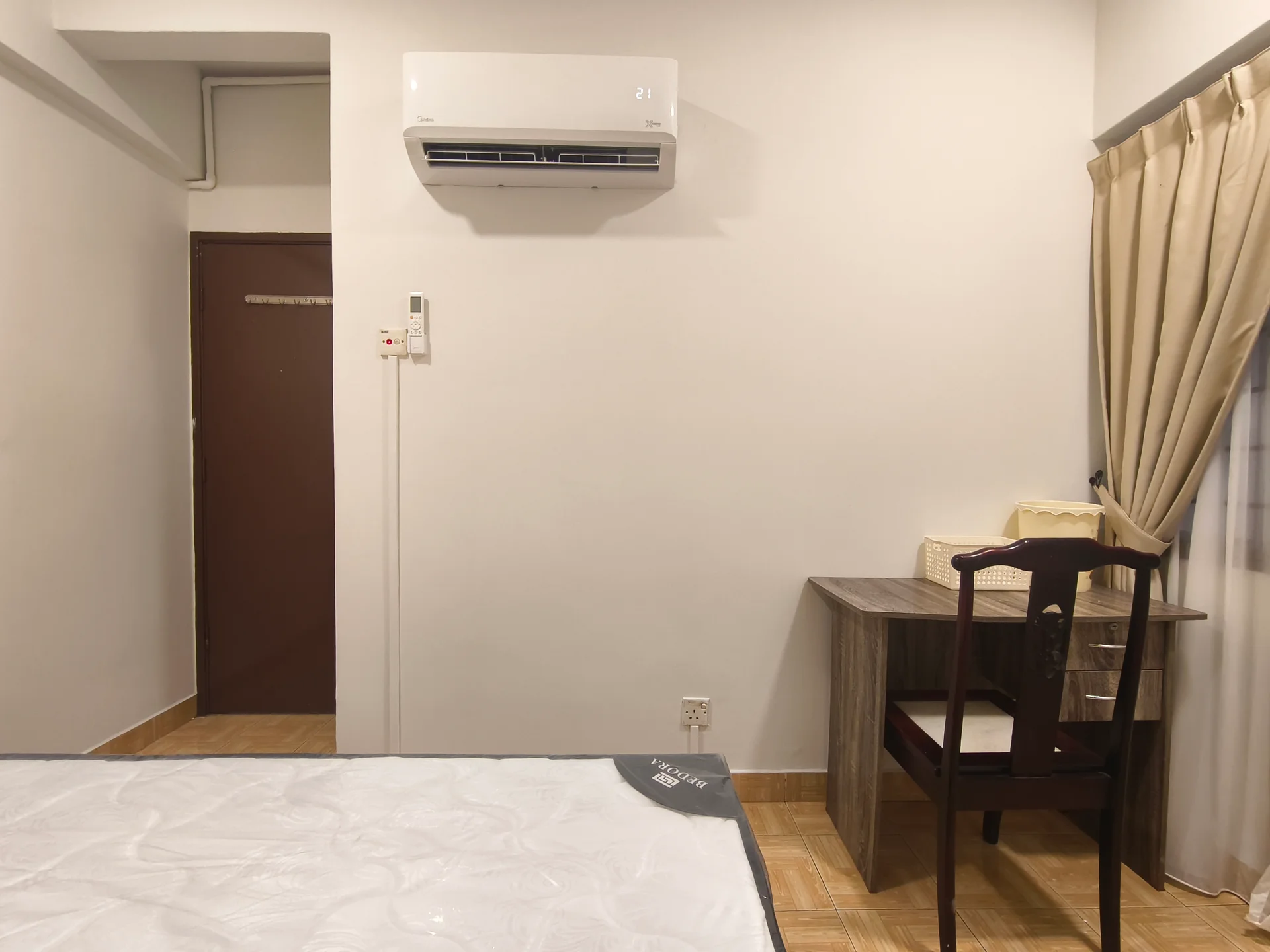 Bedroom features: single bed frame, mattress, wooden desk, wooden chair, wall-mounted split AC, curtains, light-colored walls, tile flooring, door, window; style: minimalist.