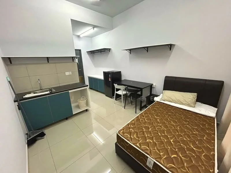 Room features: single bed with brown mattress, black upholstered headboard, white wall, grey tiled flooring, kitchenette with grey countertop, blue cabinetry, sink, refrigerator, small dining table with two white chairs, open shelving above the kitchenette, wall-mounted lighting; style: modern.