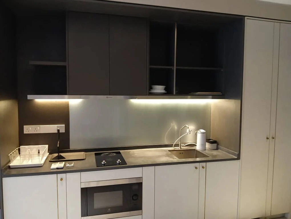 Kitchen features: grey cabinetry with gold handles, concrete countertop, built-in microwave, stainless-steel sink, chrome pull-down faucet, induction cooktop, under-cabinet lighting, open shelving, dish rack, white plates on shelf; style: modern.