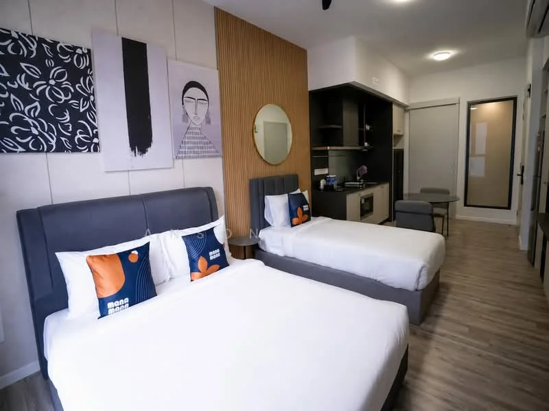 Bedroom features: two queen-size beds with upholstered headboards, decorative pillows with abstract patterns, wooden accent wall, round mirror above bedside table, wall-mounted artwork, laminate flooring, built-in cabinetry, small kitchenette with sink and microwave, recessed ceiling lights, window with sheer curtains; style: modern.