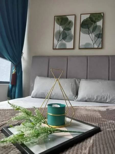 Bedroom features: queen-size bed, upholstered headboard in grey, two grey pillows, decorative tray on bed, green candle in holder, fern plant decoration, framed artwork with botanical prints, curtains in dark blue, window with natural light, neutral wall color, bedspread in light color; style: modern.