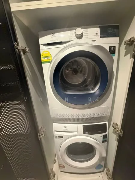 Laundry features: stacked front-load washing machine, front-load dryer, white appliances, metal cabinet doors, black perforated cabinet, built-in cabinetry, vent for dryer, energy efficiency labels on appliances; style: modern.