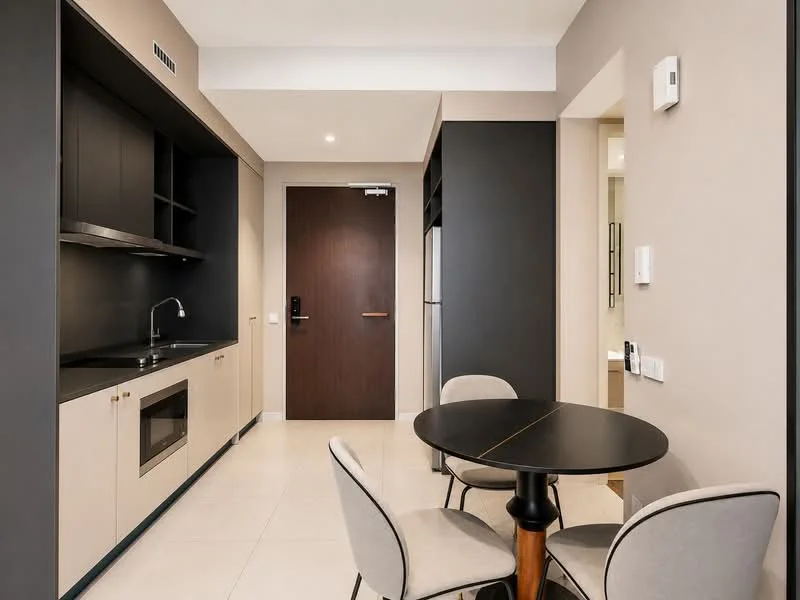 Kitchen features: black cabinetry, cream cabinetry, stainless-steel sink, chrome faucet, built-in microwave, built-in oven, refrigerator, dining table, 4 upholstered dining chairs, white tiled flooring, recessed lighting, wall-mounted light switch, door to hallway; style: modern.
