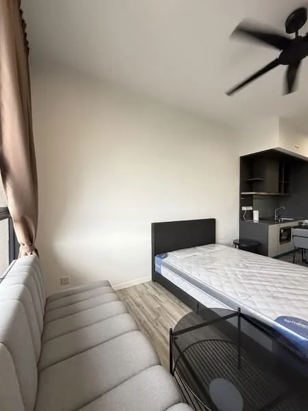 Room features: grey fabric sofa, black metal coffee table, queen-size bed with mattress, light wood flooring, white painted walls, ceiling fan, kitchenette with dark cabinetry, countertop with sink, window with brown curtains; style: modern.
