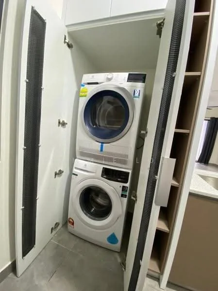 Laundry features: stacked front-load washing machine, front-load dryer, white appliances, built-in cabinetry, grey tiled flooring, ventilation grille, shelving unit, light-colored cabinetry; style: modern.