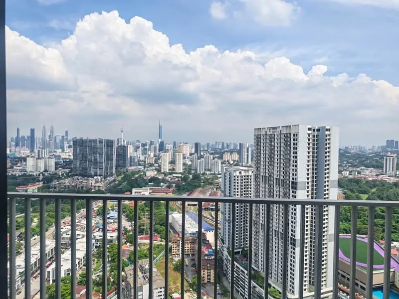 Exterior type: high-rise condominium; features: city skyline view, balcony railing, surrounding urban landscape, multiple high-rise buildings, greenery in the foreground, clear blue sky, clouds, distant landmarks; style: modern.