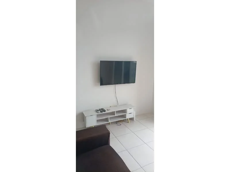 Living features: white painted walls, ceramic tile flooring, wall-mounted TV, white TV console, remote controls on console, brown fabric sofa.