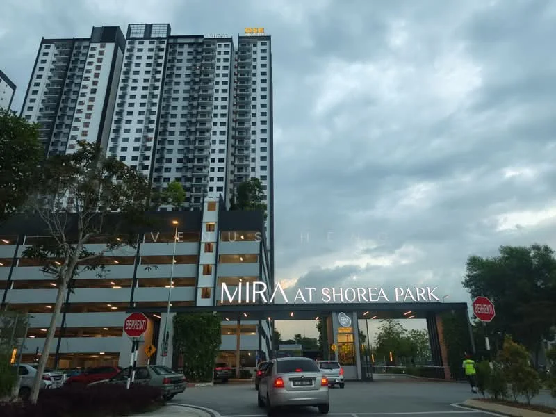 Exterior type: high-rise condominium; features: glass curtain wall, white painted facade, multi-storey car park, landscaped entrance, signage with building name, surrounded by greenery, driveway with interlocking pavers; style: modern.