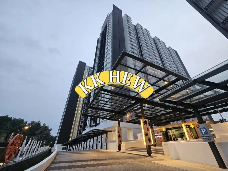Exterior type: high-rise condominium; features: glass canopy entrance, modern facade with dark cladding, paved driveway, landscaped area with decorative elements, visible parking area, multiple storeys, lighting fixtures along the entrance, surrounding greenery; style: modern.