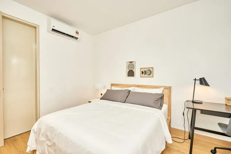Bedroom features: queen-size bed with white bedding, wooden bed frame, 2 grey accent pillows, 1 bedside lamp with black shade, study desk with black finish, wall-mounted air conditioning unit, light wood flooring, white painted walls, framed artwork on wall, woven basket on desk; style: modern.