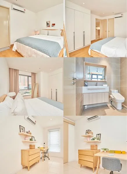 Bedroom features: queen-size bed with white bedding, light blue throw blanket, wooden bed frame, built-in wardrobe with sliding doors, wooden flooring, 1 wall-mounted split AC, window with sheer curtains, decorative wall shelves, study desk with chair, framed artwork on wall; style: modern; view: garden. Bathroom features: single-sink vanity with white cabinet, chrome basin mixer, framed mirror, one-piece toilet, tile cladding on walls, window for natural light; style: modern.