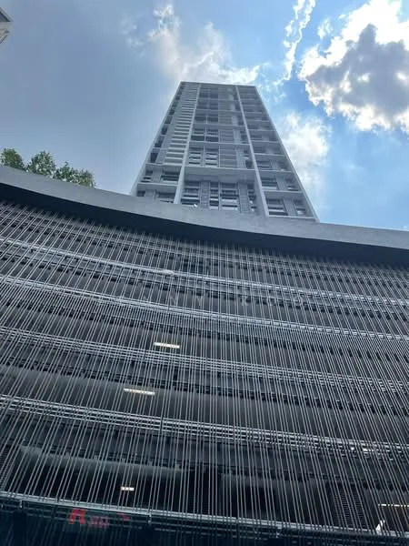 Exterior type: high-rise condominium; features: grey concrete facade, glass windows, vertical fins, multi-storey structure, open-air parking area, surrounded by greenery; style: modern.