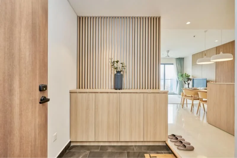 Room features: wooden entrance door, sliding door, wood panel feature wall, light wood cabinetry, decorative vase, ceramic flooring, dark stone flooring, recessed lighting, ceiling fan, open layout to living area; style: modern.