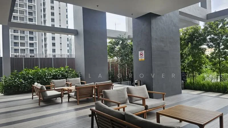 Exterior type: clubhouse; features: outdoor seating area with wooden furniture, grey concrete columns, wooden decking flooring, lush greenery with plants, surrounding high-rise buildings, signage on wall; style: modern.