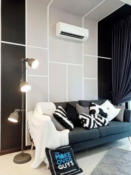 Living features: grey fabric sofa, black and white patterned cushions, floor lamp with adjustable arms, white throw blanket, black accent wall with geometric design, light grey painted walls, air conditioning unit, black curtains; style: modern.