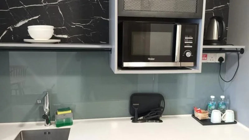 Kitchen features: black marble backsplash, white countertop, stainless-steel sink, chrome faucet, built-in microwave, kettle, two bottles of water, cups and saucers, open shelving, wall-mounted power outlet; style: modern.