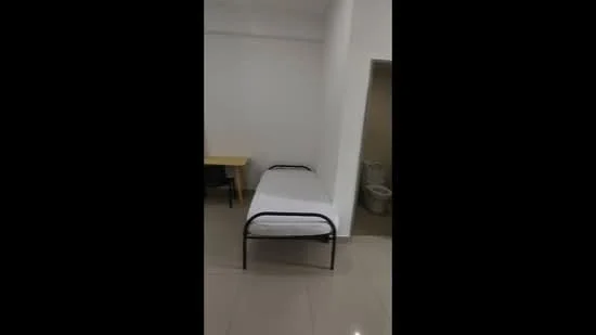 Bedroom features: single bed with metal frame, white mattress, plain white walls, glossy tile flooring, desk with black legs, doorway leading to bathroom, natural light from window, minimalist decor; style: minimalist.