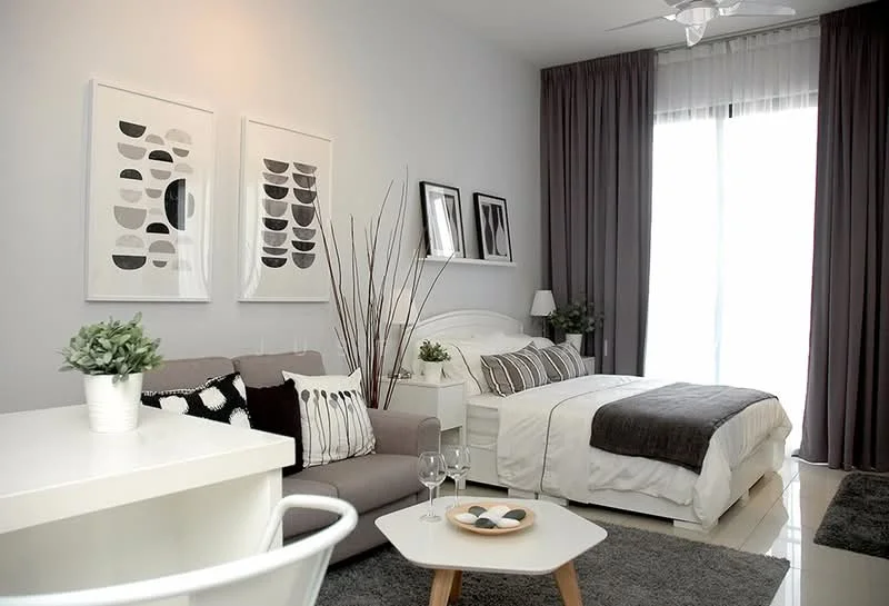 Bedroom features: queen-size bed with white bedding, upholstered headboard, 2 bedside lamps, 3-seater fabric sofa in grey, decorative throw pillows, framed artwork on walls, floor-to-ceiling windows with sheer curtains, dark grey area rug, white side table, decorative branches in vase, wall-mounted artwork, grey throw blanket on bed; style: modern.