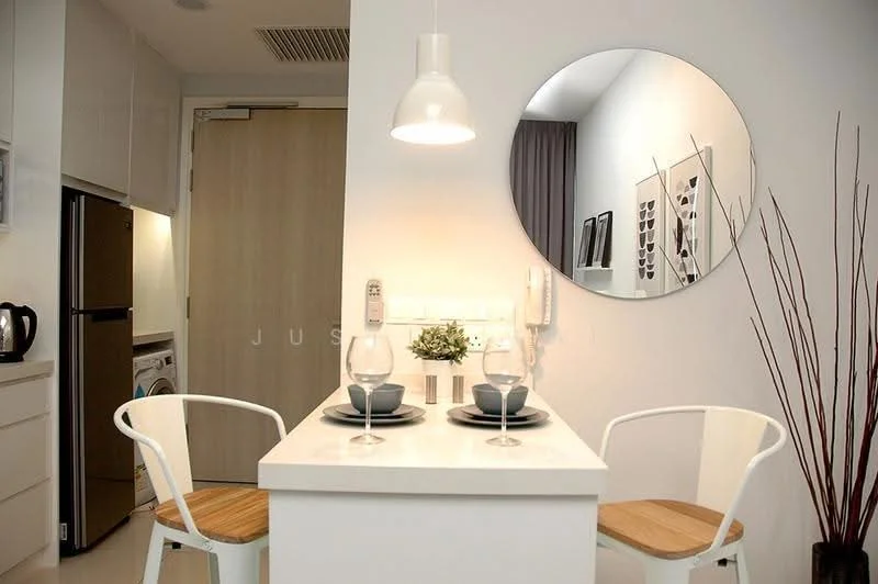 Dining features: white painted walls, white ceiling, pendant lamp, round mirror, 2 white dining chairs with wooden seats, small dining table with white surface, decorative plant in pot, glassware on table, tableware including plates and cutlery, built-in cabinetry, kitchen appliances visible in background, washing machine visible in background; style: modern.