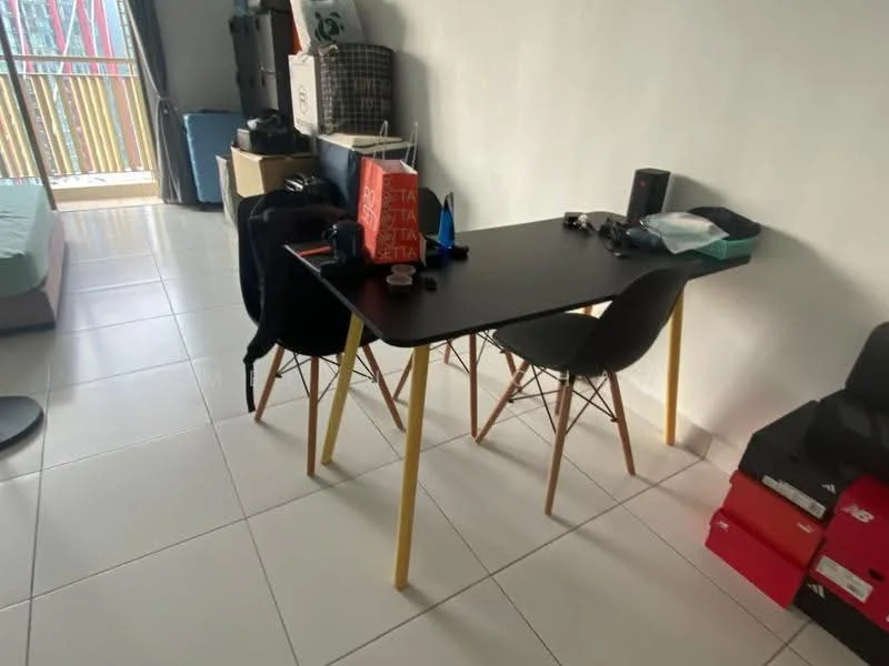 Room features: white painted walls, white tiled flooring, black table with wooden legs, two black chairs with wooden legs, various personal items on the table, window with sheer curtains, visible outdoor balcony, boxes stacked in the corner; style: modern; view: city.