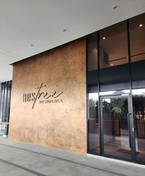 Exterior features: modern facade, textured wall finish, large glass entrance doors, overhang above entrance, interior lighting visible, paved walkway, landscaped area visible, signage with name 'NEST RESIDENCE'; style: modern.