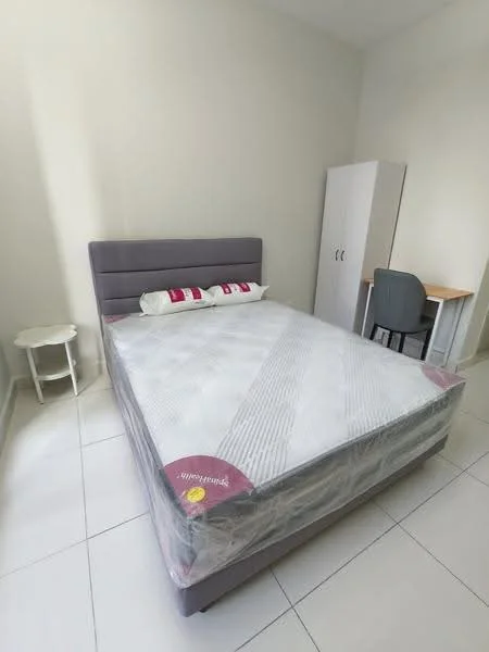 Bedroom features: queen-size bed with grey upholstered headboard, white bedding with protective plastic cover, white walls, tile flooring, built-in wardrobe with white doors, study desk with wooden top and grey legs, grey chair, small round side table, decorative pillow with red accents; style: modern.