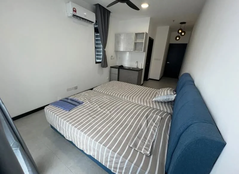 Bedroom features: two single beds with blue upholstered headboard, striped bedding in grey and white, wall-mounted air conditioning unit, ceiling fan, grey tiled flooring, black window frame with sheer curtains, small kitchenette with grey cabinets, sink, countertop, light fixture with multiple bulbs; style: modern.
