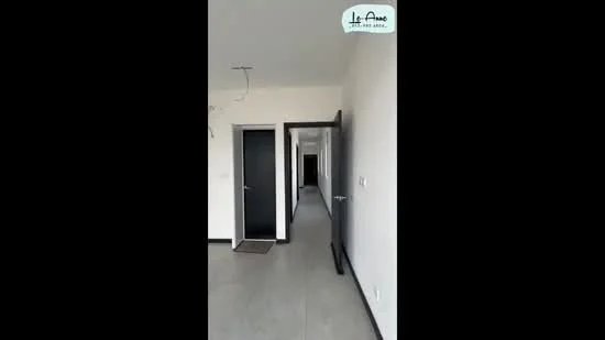 Room features: grey tiled flooring, white painted walls, black doors, door frames with black finish, ceiling with light fixtures, hallway leading to other rooms; style: modern.