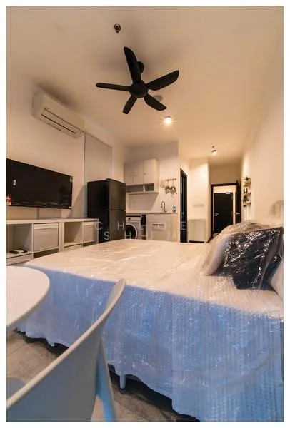 Room features: 1 wall-mounted split AC, 5-blade ceiling fan, grey laminate flooring, white painted walls, black TV console, wall-mounted TV, black refrigerator, white cabinetry, kitchenette with sink, dining table with chairs, bed with mattress covered in plastic, black door, light fixtures; style: modern.