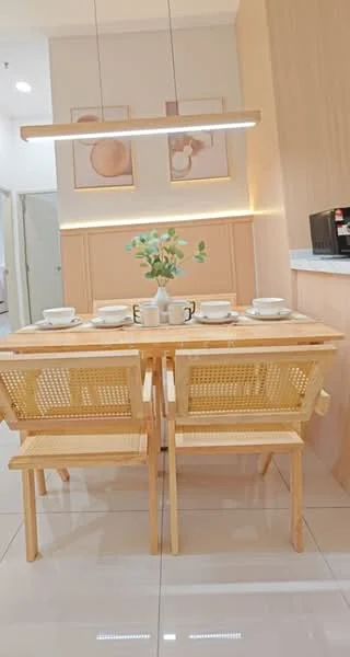 Dining features: wooden dining table, 4-seater dining table, natural wood finish, woven rattan dining chairs, decorative vase with flowers, table setting with plates and cups, wall-mounted light fixture, light wood paneling on walls, glossy tile flooring, framed artwork on walls; style: modern.