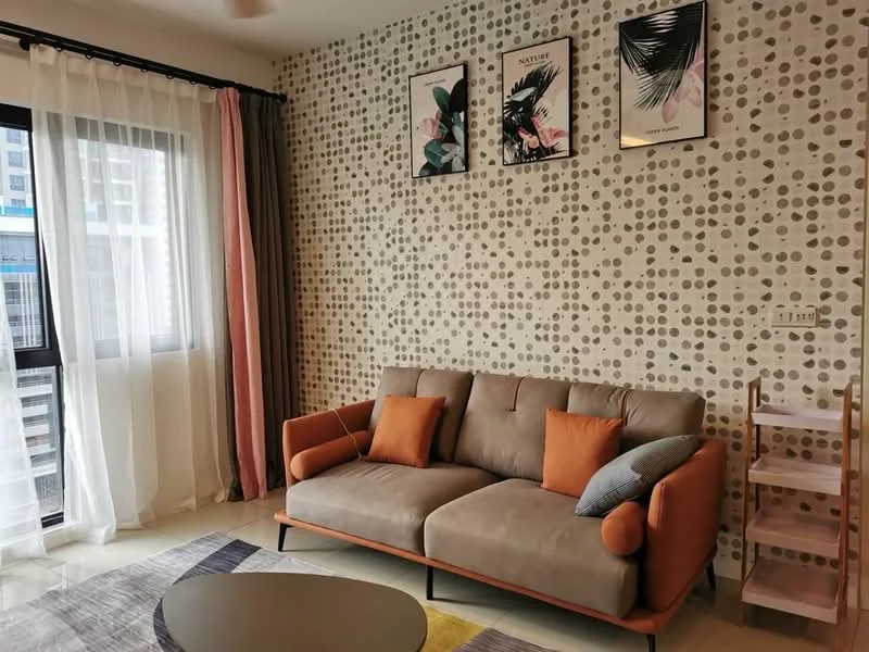 Living features: grey fabric sofa with orange accents, two decorative cushions in orange, round coffee table, polished tile flooring, floor-to-ceiling windows with sheer curtains, curtains in grey and pink, feature wall with polka dot wallpaper, framed artwork on walls, wooden shelving unit, decorative plants; style: modern; view: city.
