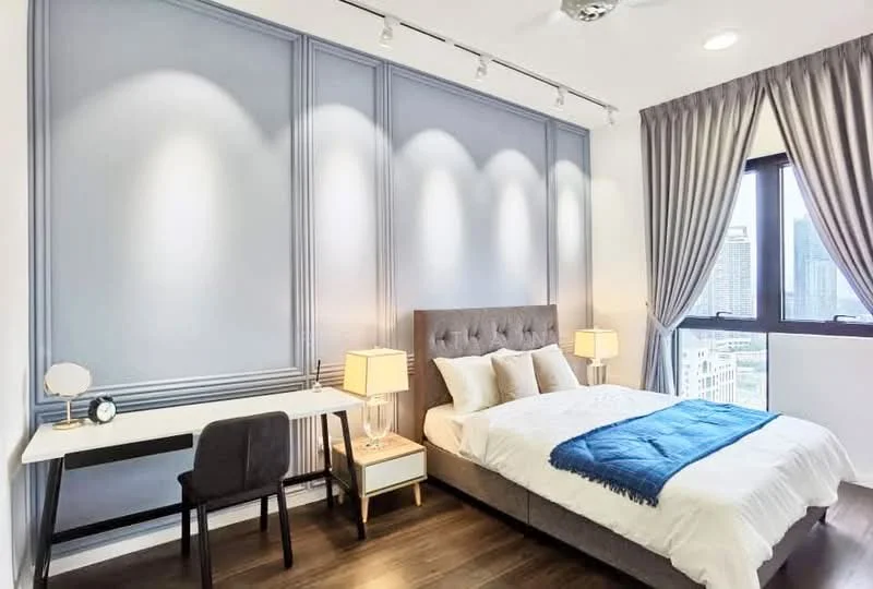 Bedroom features: queen-size bed with upholstered headboard, white bedding with blue throw blanket, two bedside lamps with white shades, study desk with white surface, black chair, grey accent wall with paneling, floor-to-ceiling windows, curtains in light grey, wooden flooring, recessed lighting, ceiling fan; style: modern; view: city.