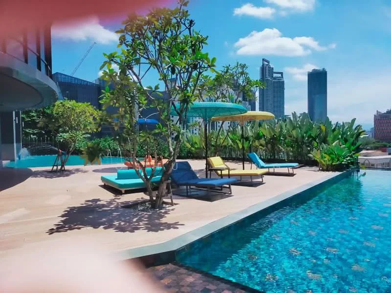 Exterior type: swimming pool deck; features: infinity pool, pool deck with loungers, tropical landscaping, manicured garden, shade umbrellas, paved walkway, city skyline view, mature trees; style: modern.