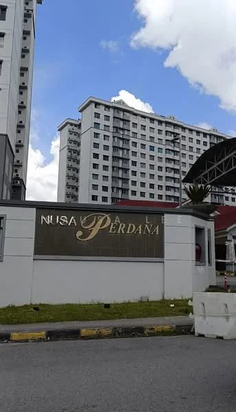 Exterior type: low-rise apartment block; features: signage with 'Nusa Perdana', white painted facade, multiple storeys, balconies visible, surrounding landscaping, paved driveway, parking area, cloudy sky, urban context; style: modern.