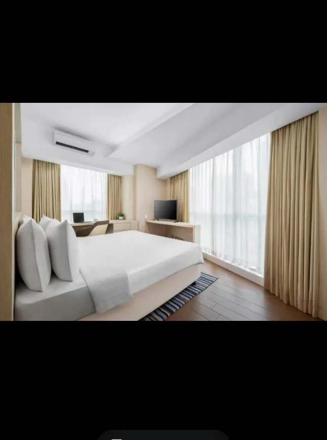 Bedroom features: king-size bed, upholstered headboard, 2 bedside pillows, wooden flooring, floor-to-ceiling windows, sheer curtains, TV console, wall-mounted TV, study desk, chair, 1 wall-mounted split AC, decorative area rug; style: modern; view: city.