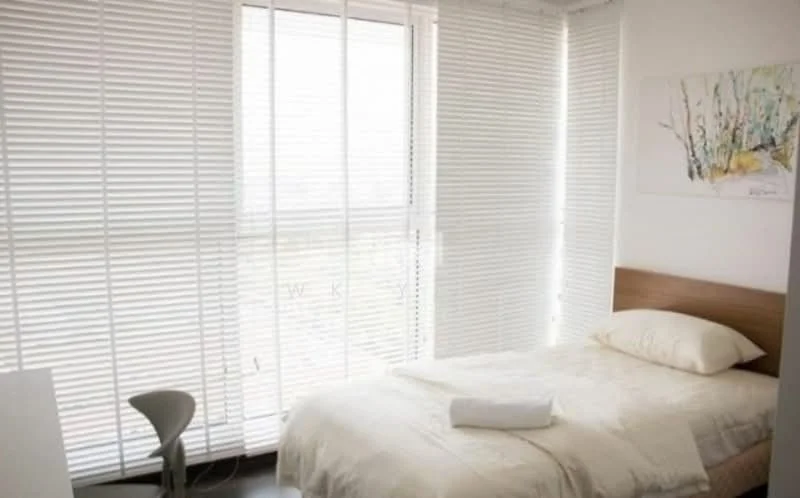 Bedroom features: single bed with white bedding, wooden bed frame, white walls, floor-to-ceiling windows, blinds on windows, laminate flooring, nightstand, table lamp, decorative artwork on wall; style: modern.